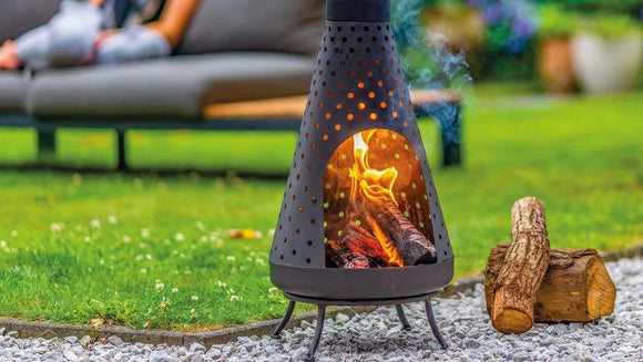 Semineu RedFire Napa aprins pe iarba, cu busteni alaturi si oameni relaxati in fundal
