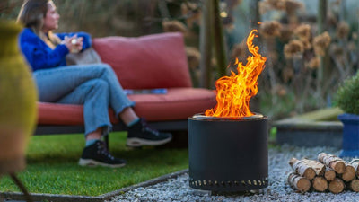 Vatra RedFire Volcano Large aprinsa, cu persoane asezate alaturi in gradina